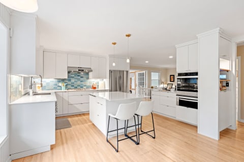 Modern kitchen with white cabinetry, blue tile backsplash, and an island with seating.