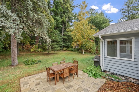 Outdoor dining set on a stone patio with greenery and trees in the background.