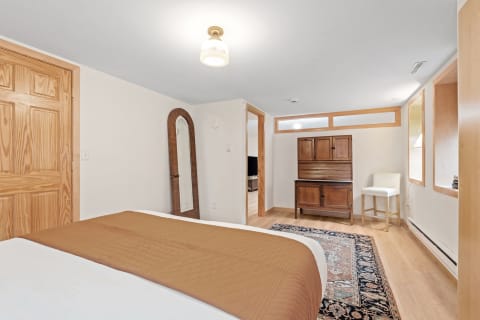 A well-lit bedroom with a made bed, wooden furniture, and decorative mirror.