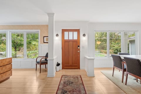 Interior of a cozy entryway featuring a wooden door, a chair, large windows, and a decorative rug.