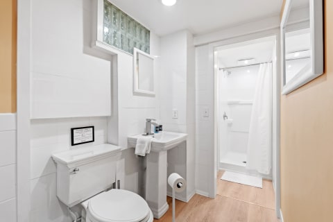 Modern bathroom featuring a white pedestal sink, toilet, and shower with a white curtain.