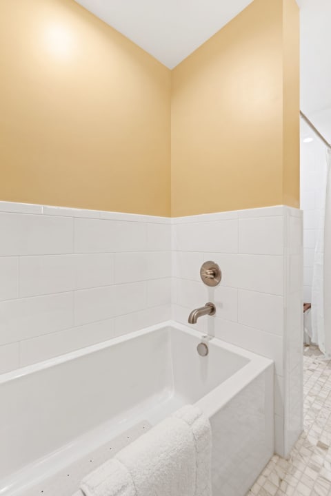 Modern bathroom corner featuring a white bathtub and yellow wall.