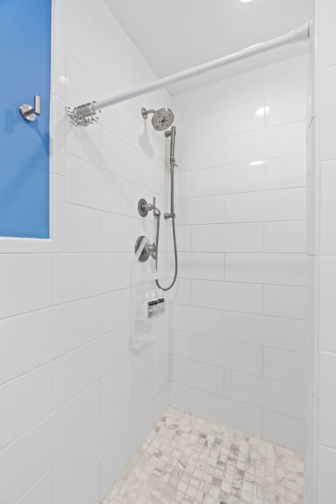 Modern shower with white tiles, chrome fixtures, and a blue window.