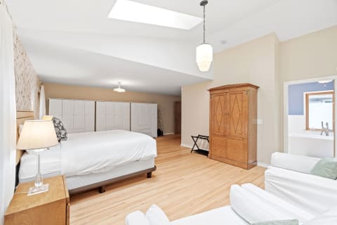 A large bedroom featuring a bed, cabinets, and a wooden armoire, illuminated by natural light from a skylight.
