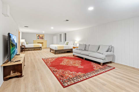 A spacious basement room featuring beds, a gray sofa, and a colorful rug.