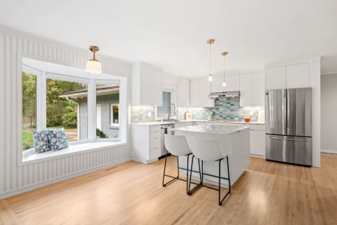 Modern kitchen with white cabinetry, blue tile backsplash, and a cozy window seat.