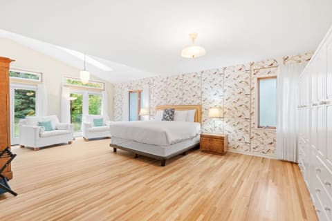 A spacious bedroom featuring a king-sized bed, white armchairs, and colorful bird-themed wallpaper.