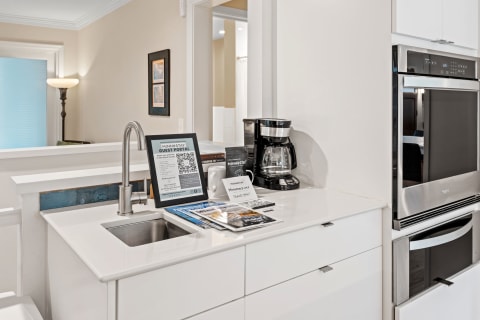 Modern kitchen with white countertop, coffee machine, and guest information stand.