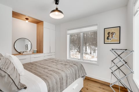 A cozy modern bedroom featuring a gray quilt and white cabinetry with a large window overlooking a snowy scene.