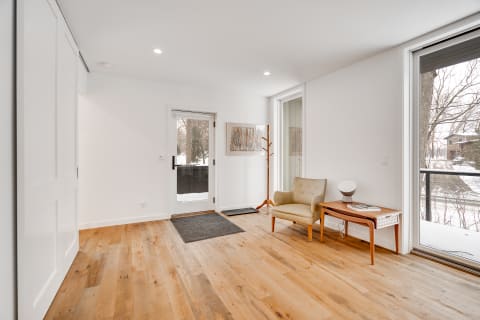 Contemporary entryway with wooden flooring, an armchair, a side table, and a coat rack.