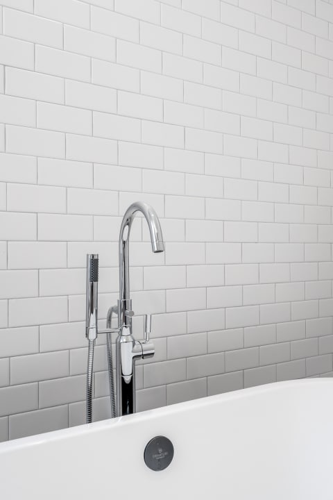 Sleek chrome faucet above a white bathtub with subway tile background.