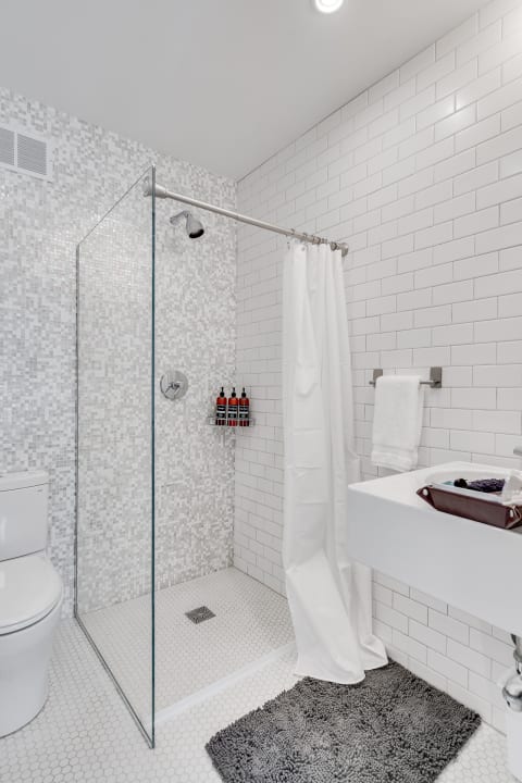 Contemporary bathroom featuring a glass shower, white sink, gray bath mat, and mosaic tiles.