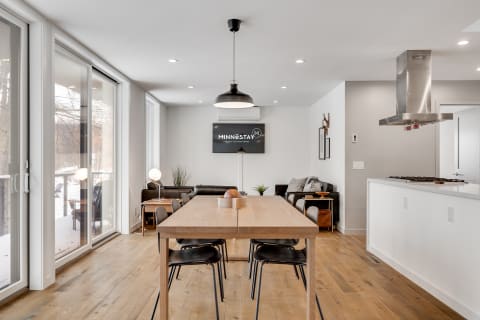 A contemporary dining area with a long wooden table, black chairs, and a cozy living room visible in the background.