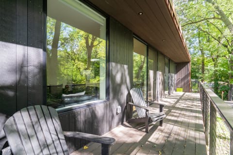 Wooden deck with two black chairs and large windows reflecting nature.