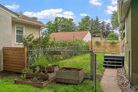 Backyard with wooden planters, a chain-link fence, and green grass under a blue sky.