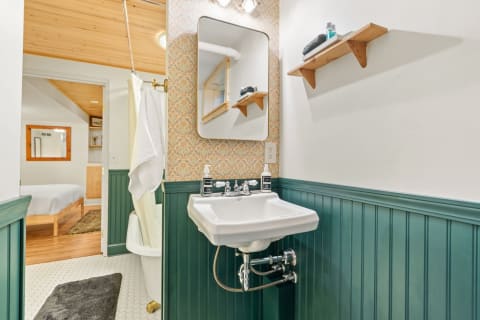 A compact bathroom with a white sink, green wainscoting, and patterned wallpaper.