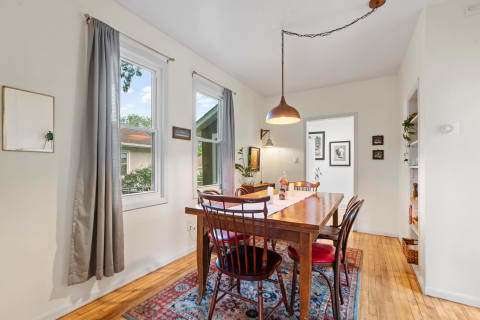 Dining room featuring a wooden table, chairs with red cushions, and sunlight from large windows.