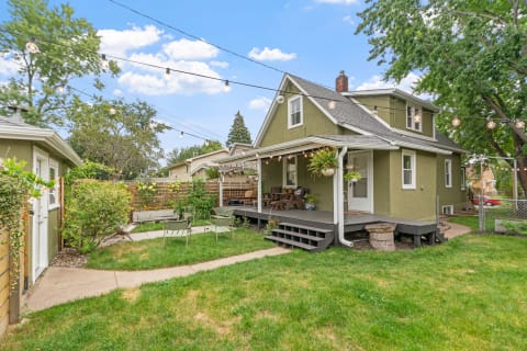 A green two-story house with a porch and a well-kept garden in a suburban setting.