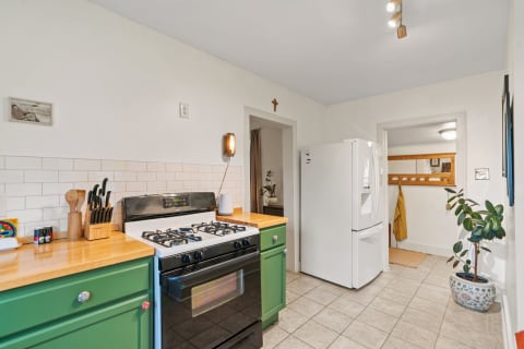 A modern kitchen with green cabinets, a gas stove, and a white refrigerator, showcasing warm lighting and decorative elements.