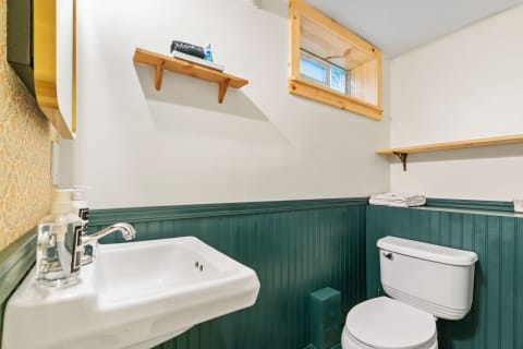 A small bathroom with a white sink, modern toilet, green wainscoting, and wooden shelves.