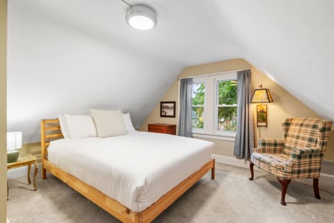 Attic bedroom featuring a wooden bed, plaid chair, and large windows with a view.
