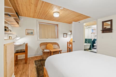 Interior of a cozy bedroom with wooden features, a small desk, and a bathroom entrance.