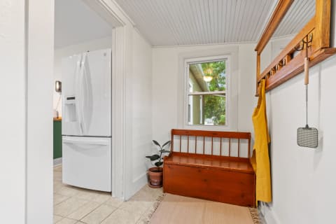 Entryway with a white refrigerator, wooden bench, and yellow apron hanging on hooks.
