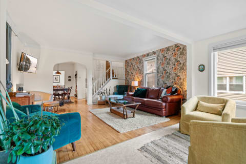 A vibrant living room with a floral accent wall, a burgundy sofa, teal accents, and a dining area visible in the background.