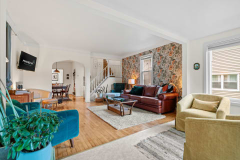 Spacious living room with floral wallpaper, leather sofa, and teal armchair.