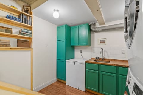 Compact laundry space with teal cabinets, wooden countertop, and vintage books.