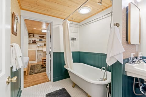 A vintage-style bathroom with a white clawfoot bathtub, green wainscoting, and a modern mirror above the sink.