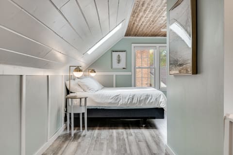 Clean and modern attic bedroom featuring a sloped ceiling, bed, and decorative elements.