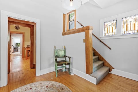A cozy hallway leading to a staircase with stained glass windows and a green chair.