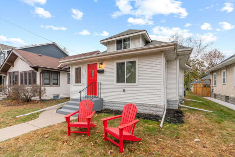 A charming house with a red door and two red Adirondack chairs in front yard.