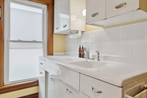 A bright kitchen featuring a white sink, white cabinets, and a window with frosted panes.