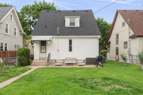 A cozy two-story house with a green door, outdoor seating, and a grill in the backyard.