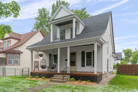 Two-story house with a white exterior, slate-colored roof, and a porch featuring hanging chairs.