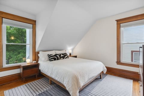 A stylish bedroom with sloped ceiling, white bedding, and wooden accents.