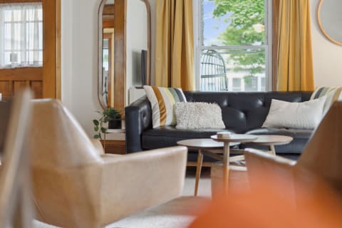 A well-decorated living room with a black leather sofa, yellow curtains, and a round wooden coffee table.
