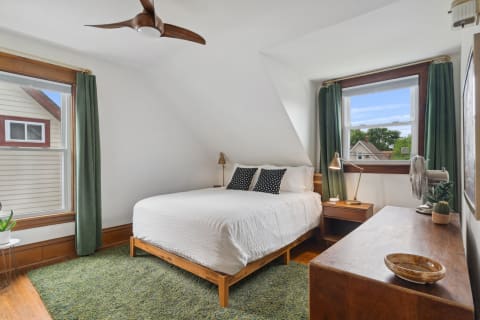 Modern bedroom featuring a white bed, green curtains, and decorative wooden elements.