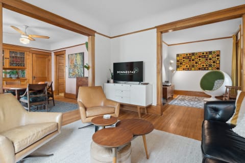 A cozy living room featuring tan leather chairs, a white TV console, and colorful artwork.