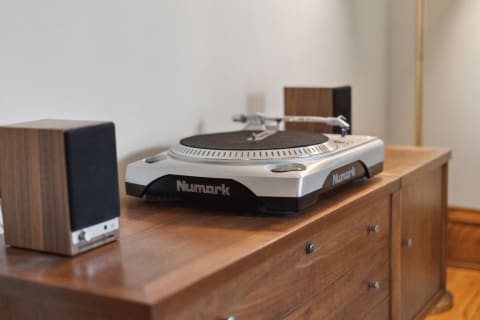 A Numark turntable with compact wooden speakers on a wooden surface.