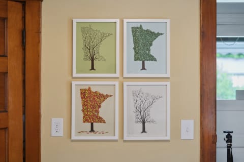Four framed tree artworks representing different seasons on a beige wall.