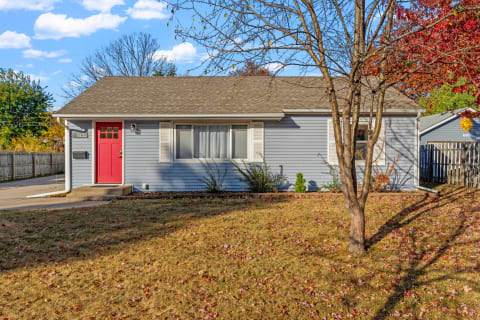 Single-story house with a red door in autumn leaves.
