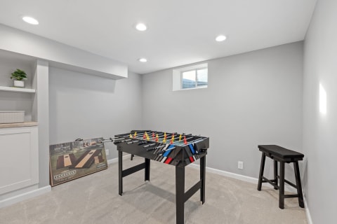 A modern game room with a foosball table and cornhole game propped against the wall.