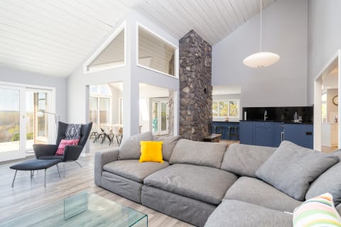 A contemporary living room featuring a gray sectional sofa, a black armchair, and a stone wall, with large windows providing scenic views.