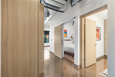 A modern corridor with a sliding door opening into a stylish bedroom, showcasing polished concrete floors and artwork.