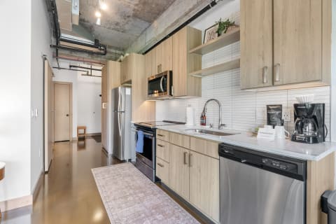 Modern kitchen with light wood cabinets, stainless steel appliances, and a decorative rug.
