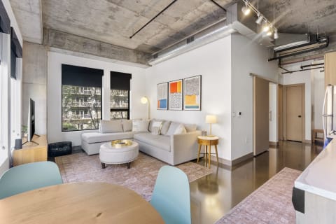 A contemporary apartment living room featuring a sectional sofa, artwork, and a dining table.