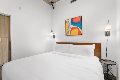 Modern bedroom with white bed linens and abstract wall art.